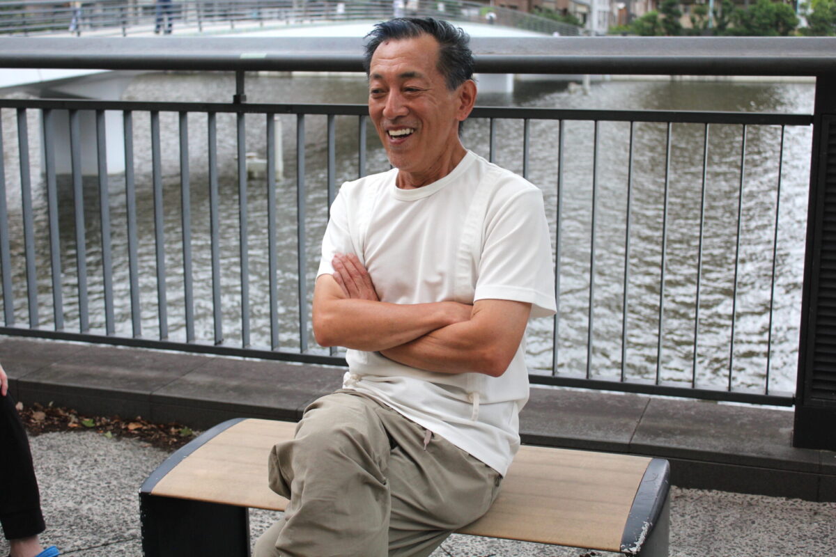 ベンチに座って笑顔でインタビューに答える山田ゴメスさんの画像